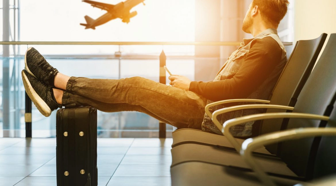 man sitting on gang chair with feet on luggage looking at airplane